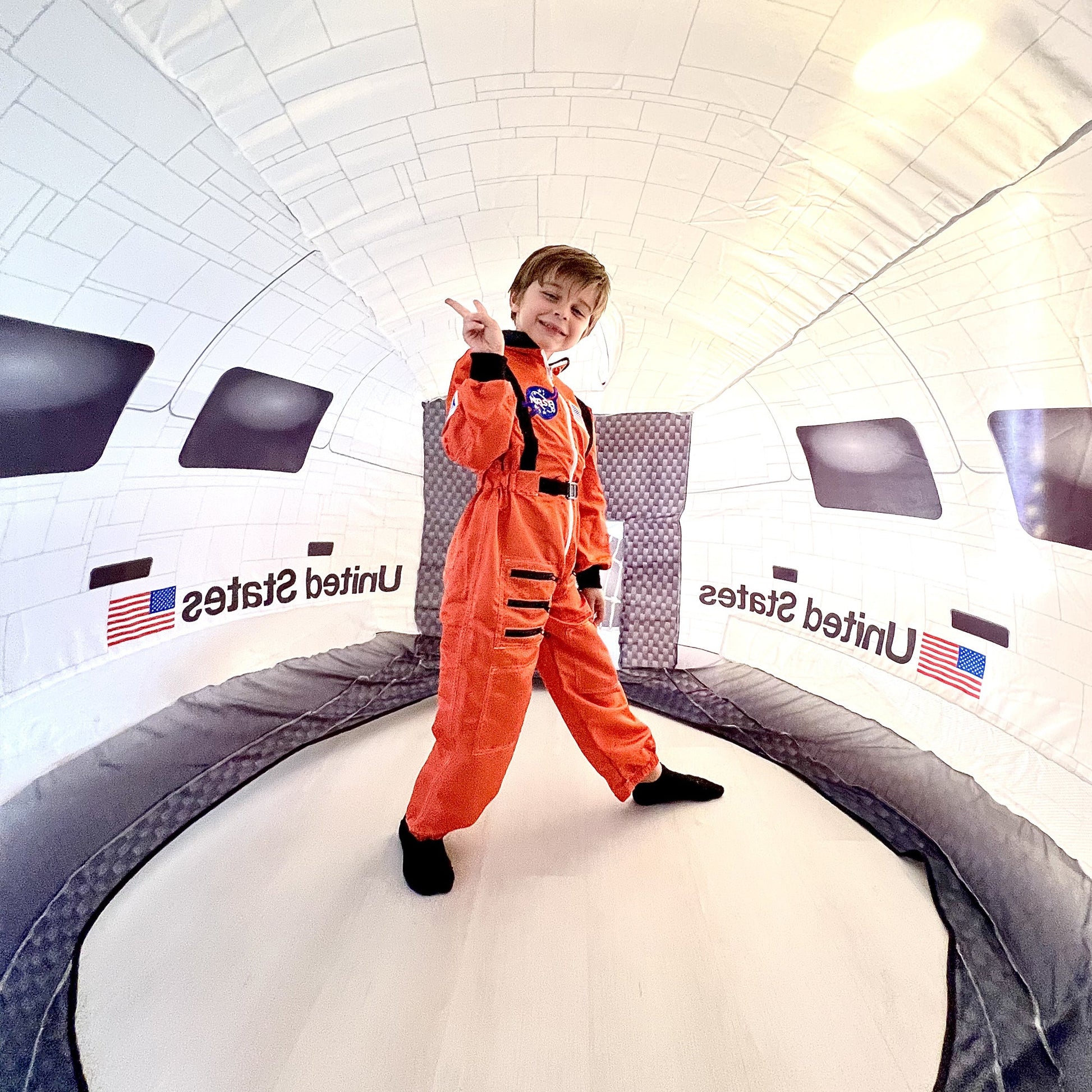 A child in an orange astronaut flight suit standing proudly inside the spacious Space Shuttle AirFort.