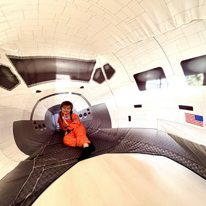 A young child sitting comfortably inside the massive, fully inflated Space Shuttle AirFort.