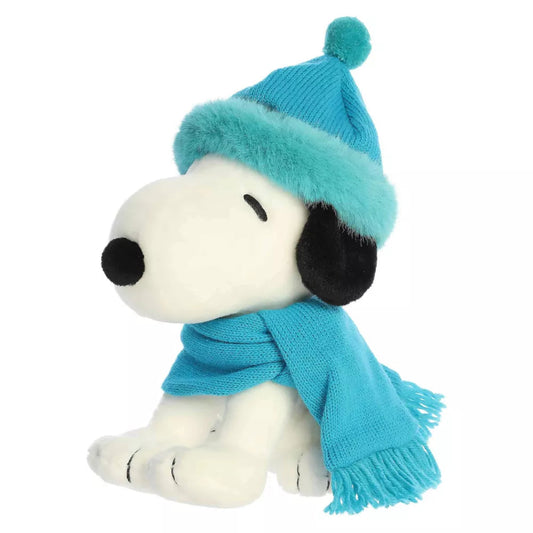 Three-quarter seated view of Aurora Peanuts Snoopy 9-inch plush toy wearing a teal winter beanie and fringe scarf.