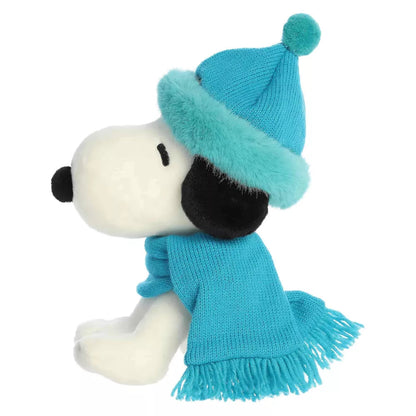 Side profile view of Aurora Peanuts Snoopy plush showing seated posture, black ear, and teal winter hat profile.