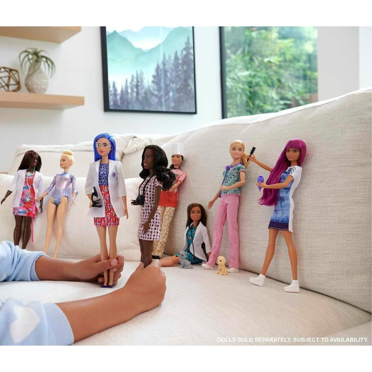 Lifestyle thumbnail showing hands playing with an assortment of Barbie career dolls on a sofa.