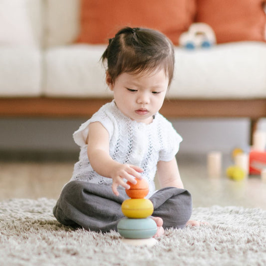 Child sitting on carpet playing with the PlanToys wooden stacking ring cups toy.