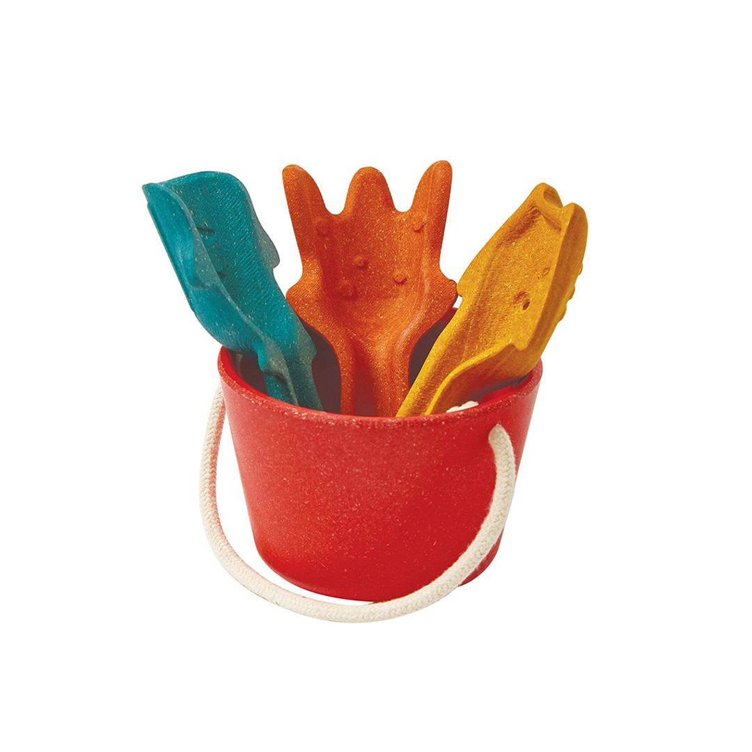 Red PlanToys sand bucket with all three colorful wooden tools stored standing inside.