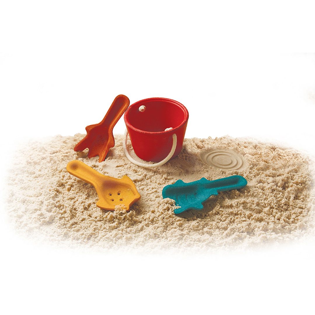 PlanToys 4-piece sand play set arranged together on soft beach sand.