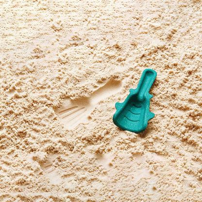Teal PlanToys wooden sand tool resting on sand beside its sand imprint.
