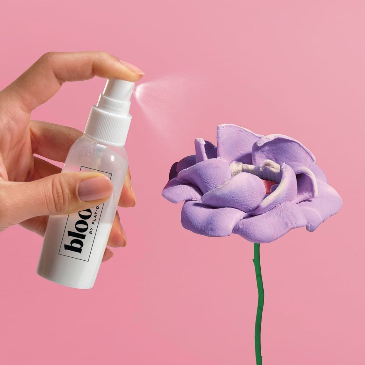 Hand spritzing preserving finishing spray onto a dried pink Play-Doh flower bloom.
