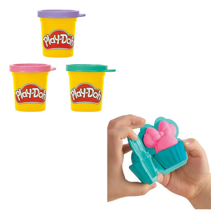 Hands-on detail thumbnail of a child pressing pink Play-Doh into a turquoise cupcake mold topped with a Minnie bow.