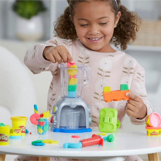 Child placing colorful Play-Doh compound into the top of the Swirlin' Smoothies toy blender.