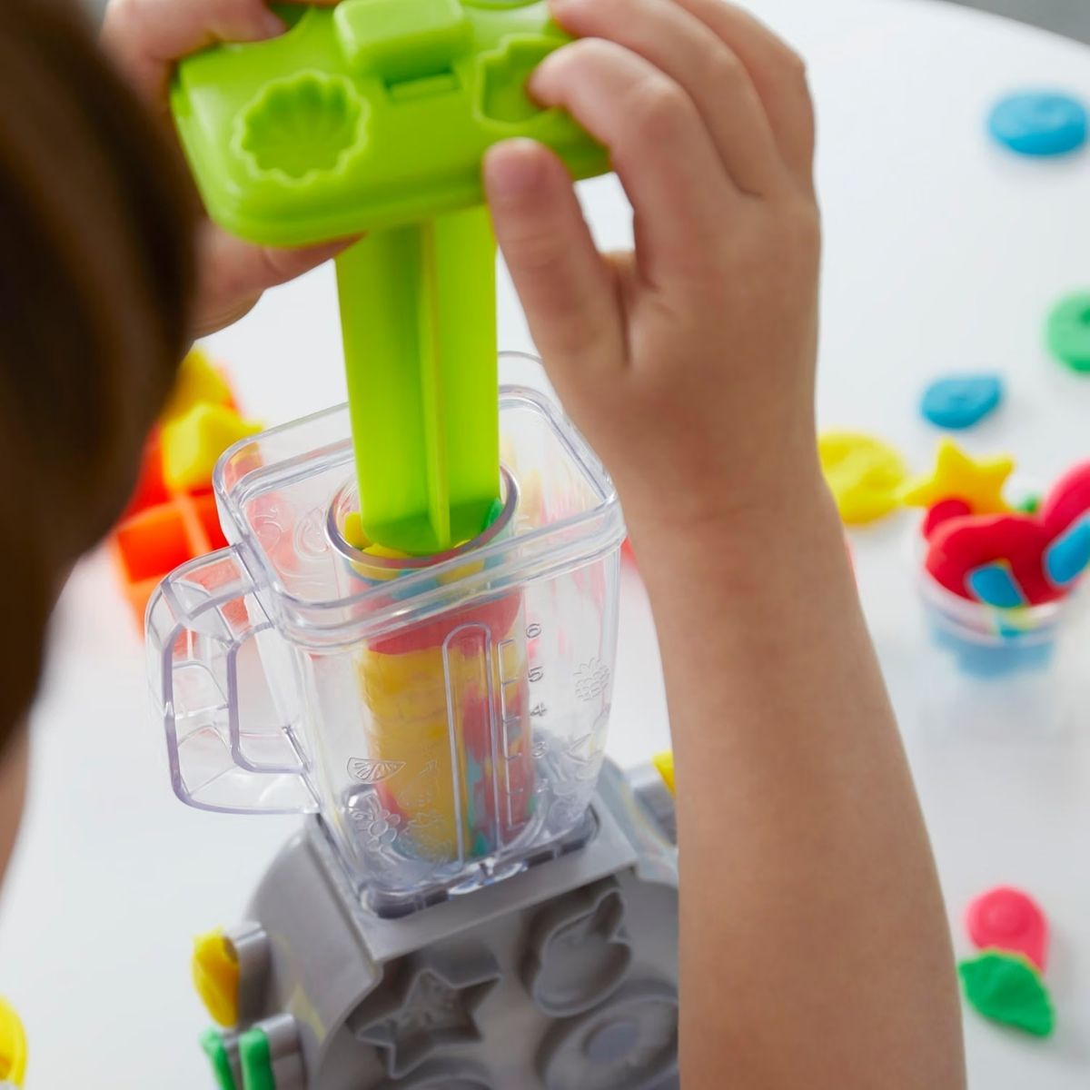 Child using the green plunger tool to press Play-Doh through the toy blender.