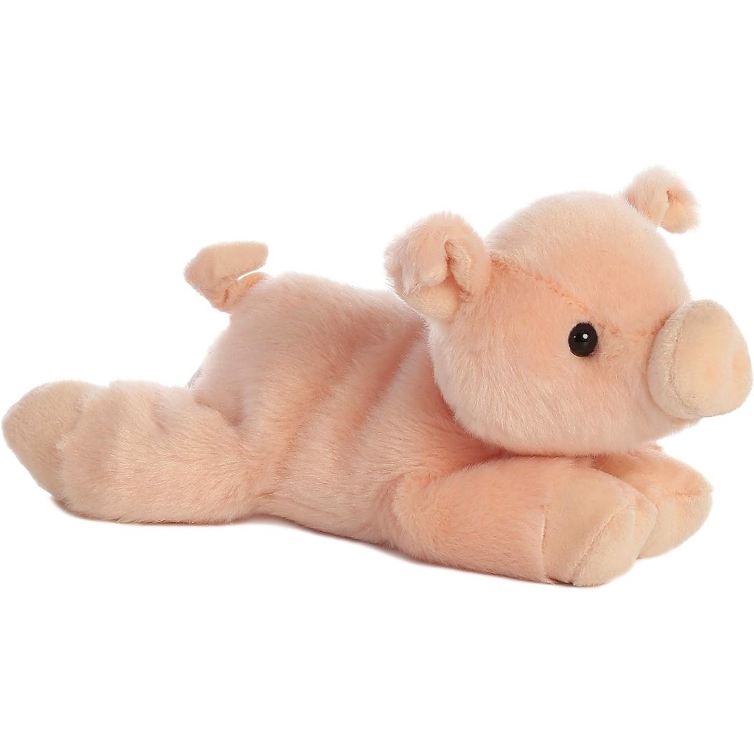 Angled view of the Aurora Mini Flopsie 8-inch Percy the Pig plush resting on its belly, showing its light pink fur and curly tail.
