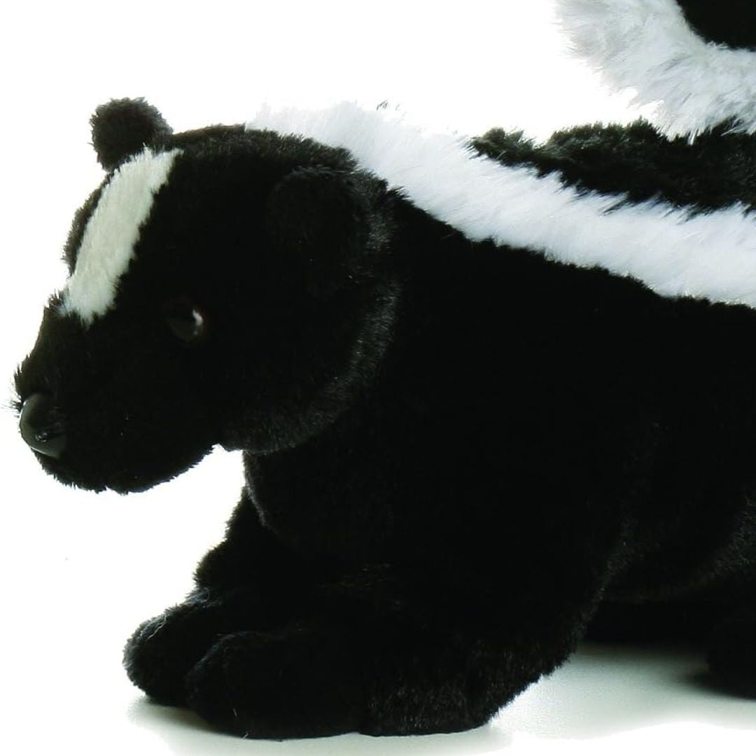 Close-up front profile of the skunk stuffed animal highlighting the white stripe on its face, dark eyes, and resting front paws.