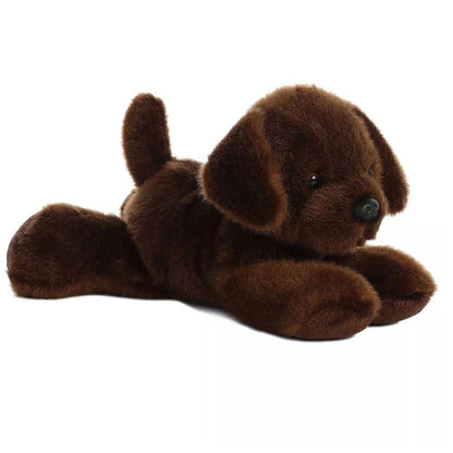 Angled front view of the 8-inch Aurora Mini Flopsie Lil Lucky Chocolate Labrador stuffed animal lying down, showing its dark brown fur and perky tail.