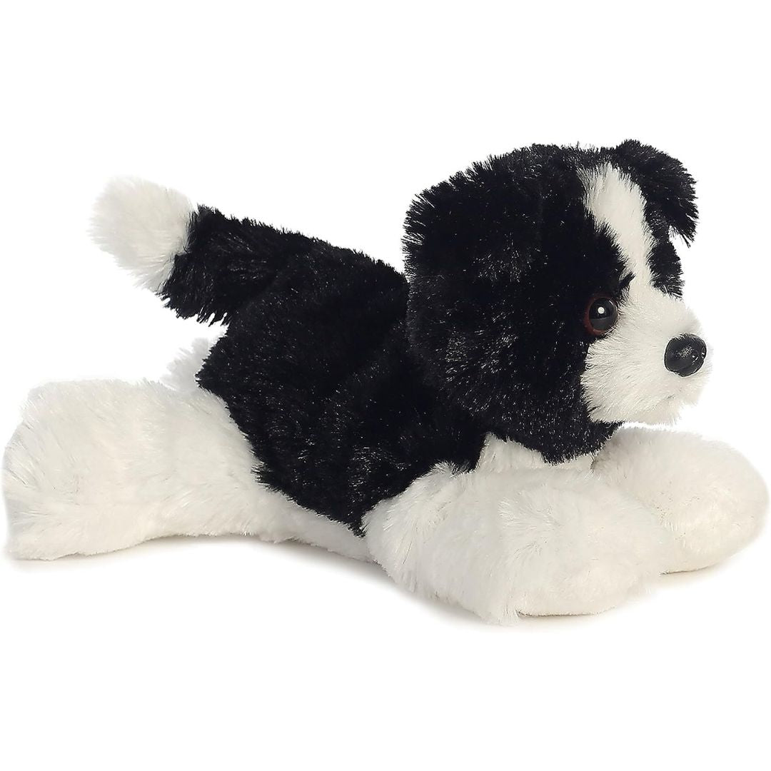 Angled side view of the Aurora Mini Flopsie Cami Border Collie 8-inch plush resting on its belly, featuring black and white fur.