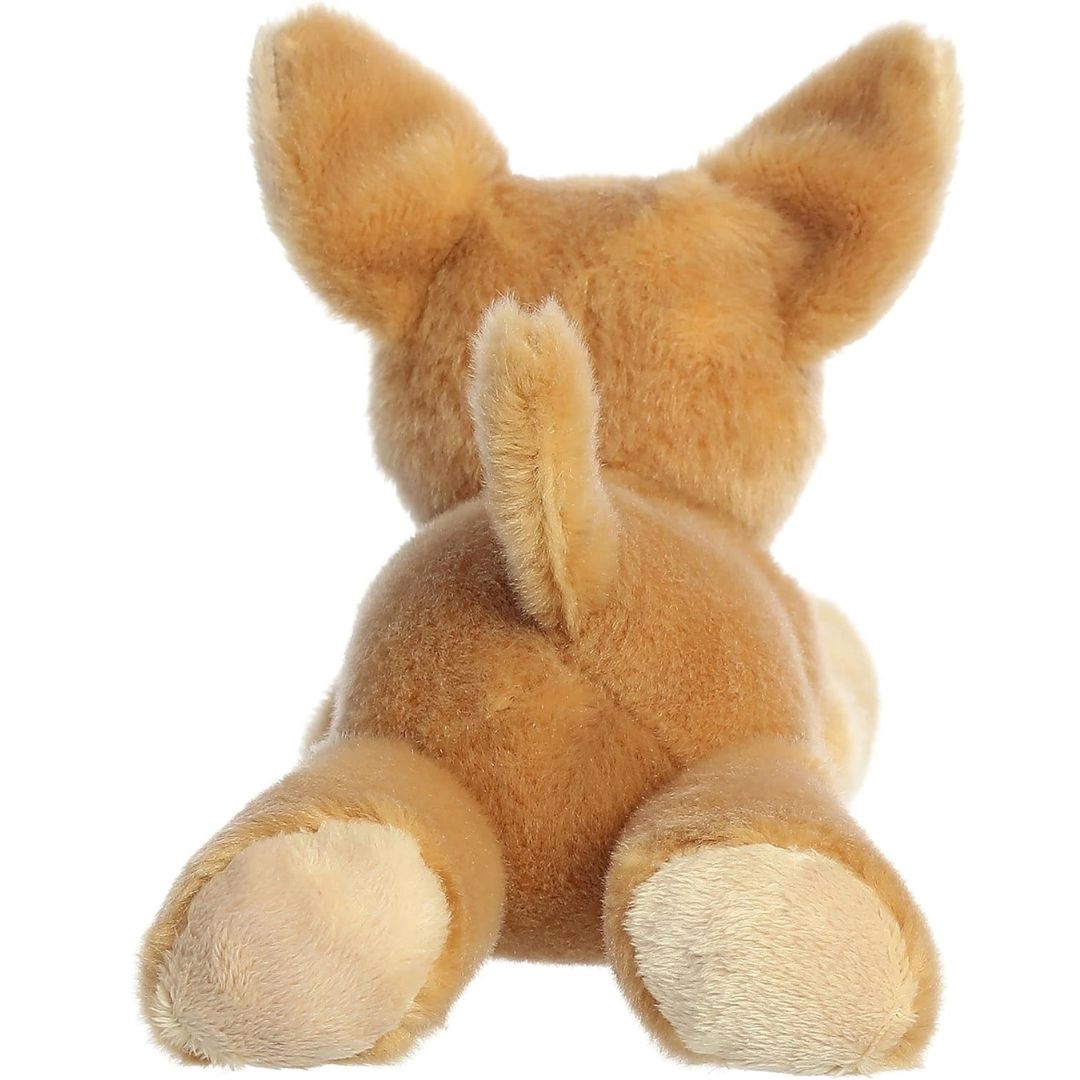 Rear view of the dog plush from behind, showing its tan back, outstretched hind legs with cream-colored paws, and a small upright tail.