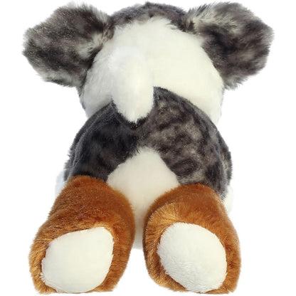Rear view of the dog plush from behind, showing its blue merle back, extended copper-tan hind legs, and white-tipped upright tail.