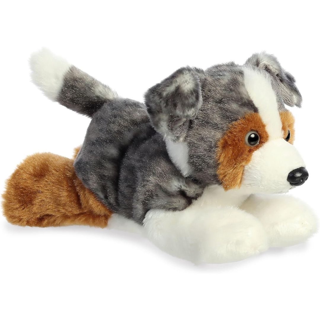 Angled side view of the Aurora Mini Flopsie Australian Shepherd 8-inch plush resting on its belly, featuring blue merle, white, and tan fur.
